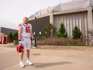 Caden Ellingson stands outside the DakotaDome. He is dressed in his football gear and holding his helmet in his right hand.