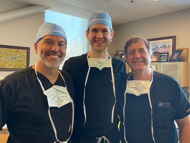 Three dentists in scrubs stand next to each other and smile for a picture.