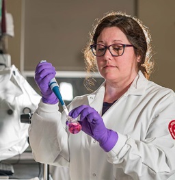 Woman in lab coat and gloves with test tube in lab.