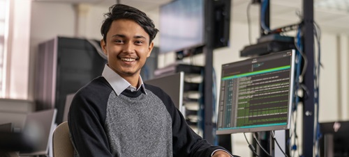 A computer science student smiling in front of his PC.