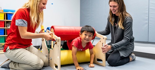 Two OT Students helping a child crawl through a developmental tool.
