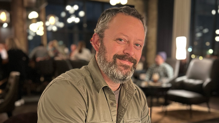 Benjamin Percy sits at dark-lit restaurant and smiles for a photo.
