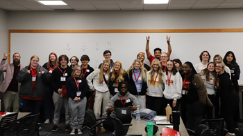 A group of nearly 20 high school Teacher Pathway students and USD faculty and staff stand together for a group photo in a classroom.